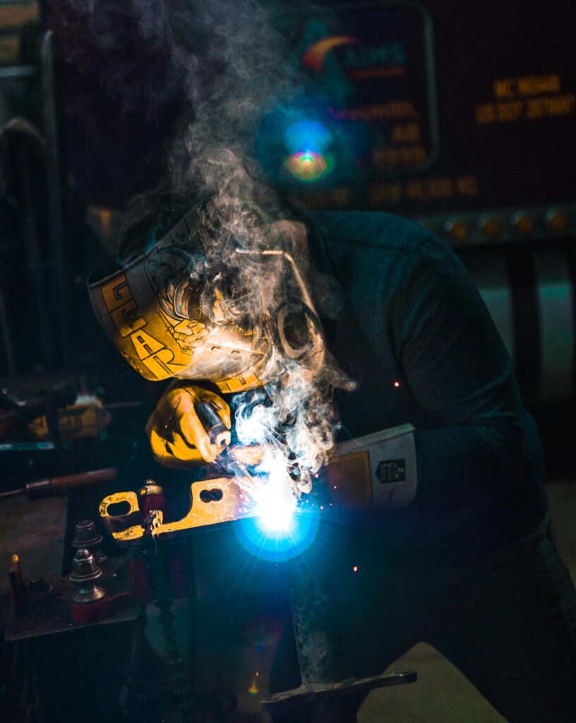 A person is welding, creating sparks and smoke, while wearing a protective helmet and working on metal.