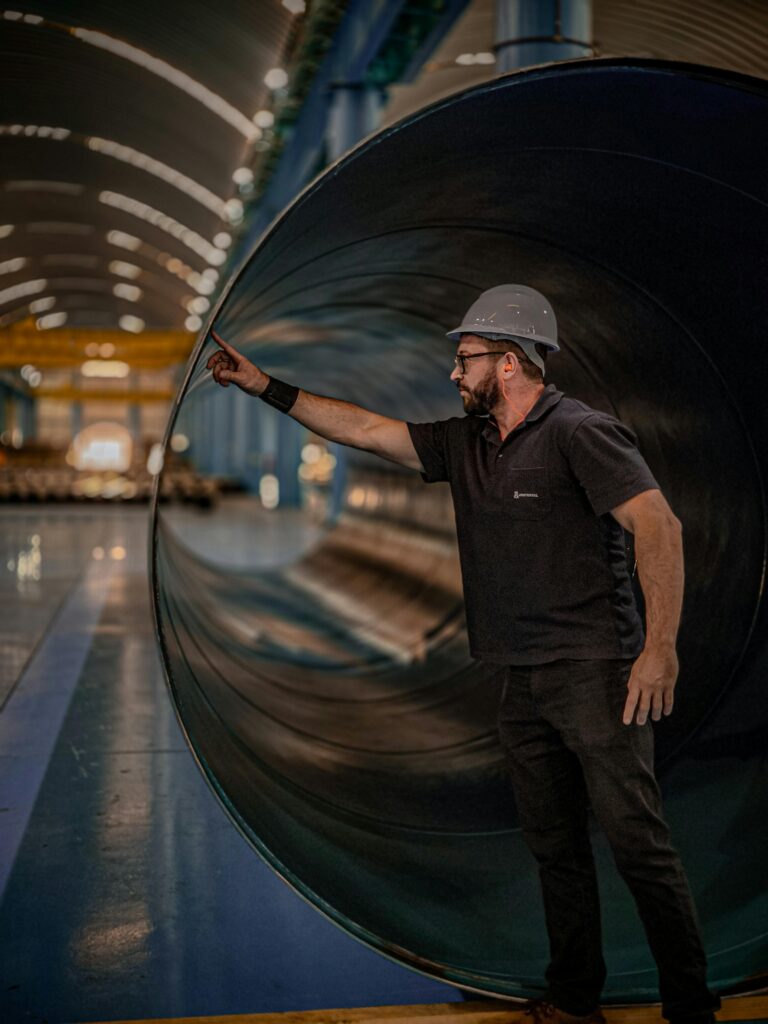 A person stands inside a large cylindrical structure in a spacious industrial facility.