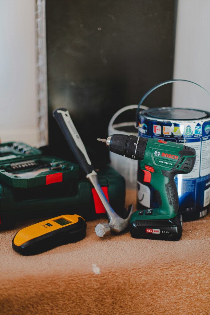 A workbench scene featuring a drill, a hammer, a measuring tool, and a can of paint.